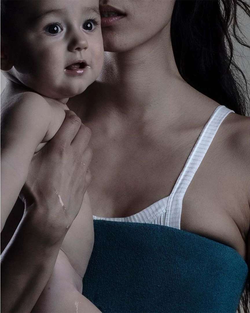 Close-up of a mother and child in a softly lit indoor setting, featuring the baby's curious expression and the mother's gentle embrace.