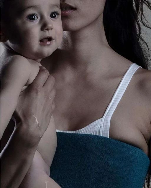 Close-up of a mother and child in a softly lit indoor setting, featuring the baby's curious expression and the mother's gentle embrace.