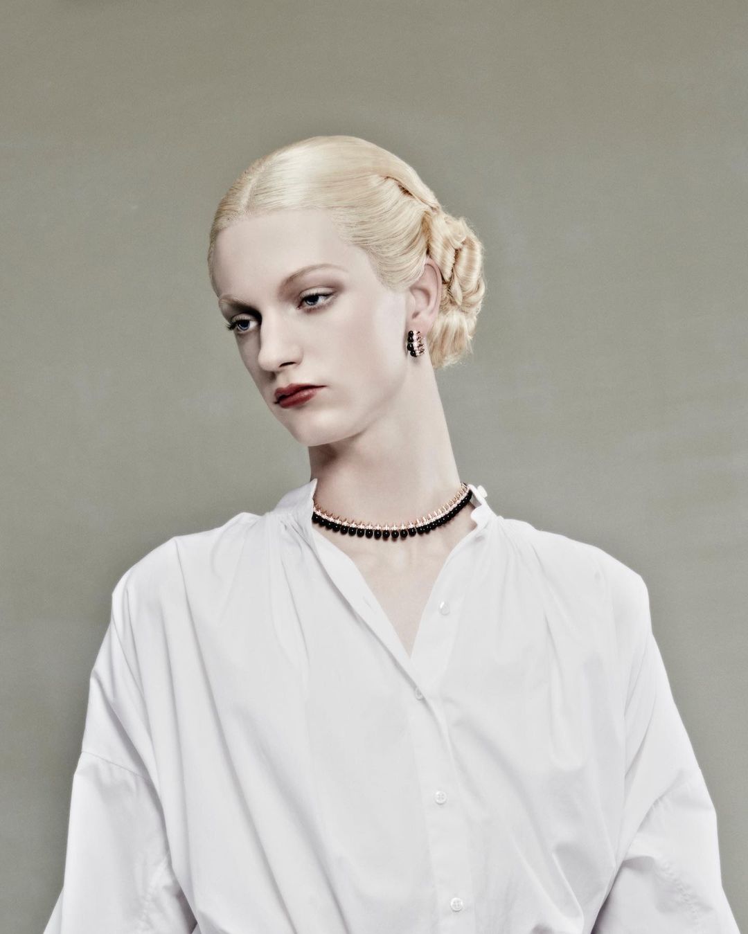 Model with platinum blonde braided hair in a white shirt and dark choker necklace against a grey backdrop by Jet Swan.