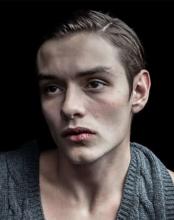 Close-up portrait of a young man wearing a grey knitted tank top against a dark background by Jet Swan