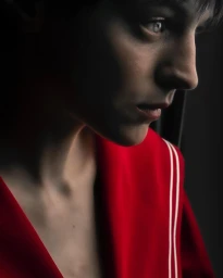Close-up profile portrait of a person in a bright red garment with white stripes against a dark background.