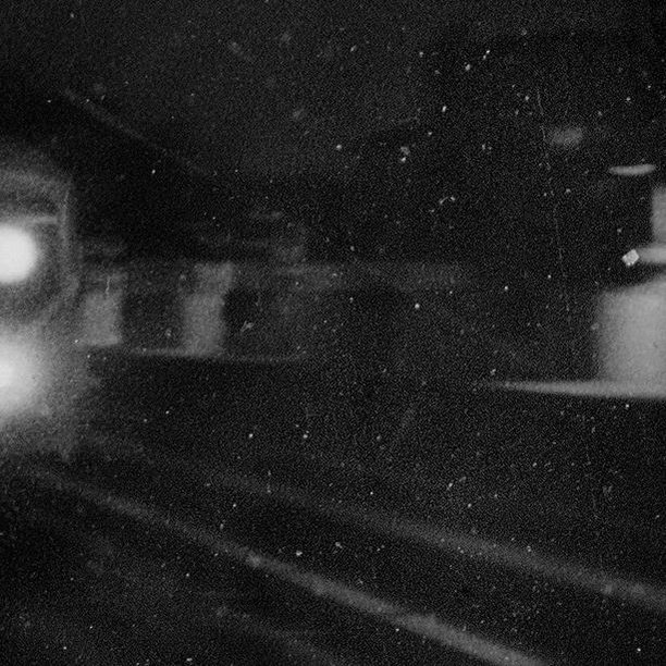 Black and white grainy photograph of an out-of-focus train station platform and train, highlighting the gritty, vintage aesthetic.