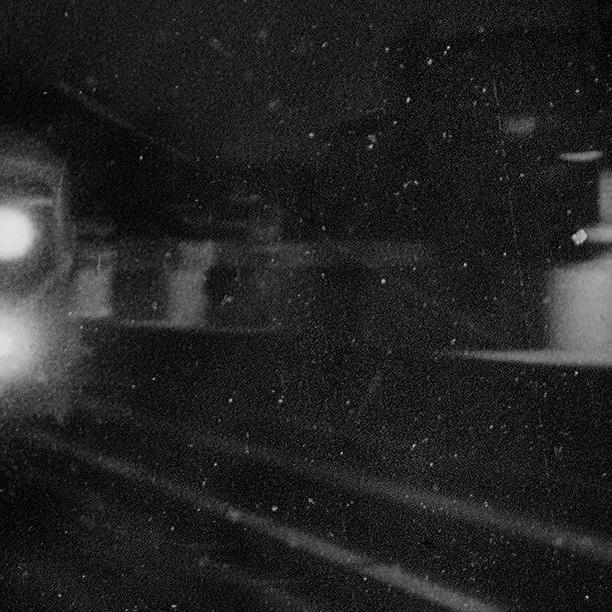 Black and white grainy photograph of an out-of-focus train station platform and train, highlighting the gritty, vintage aesthetic.