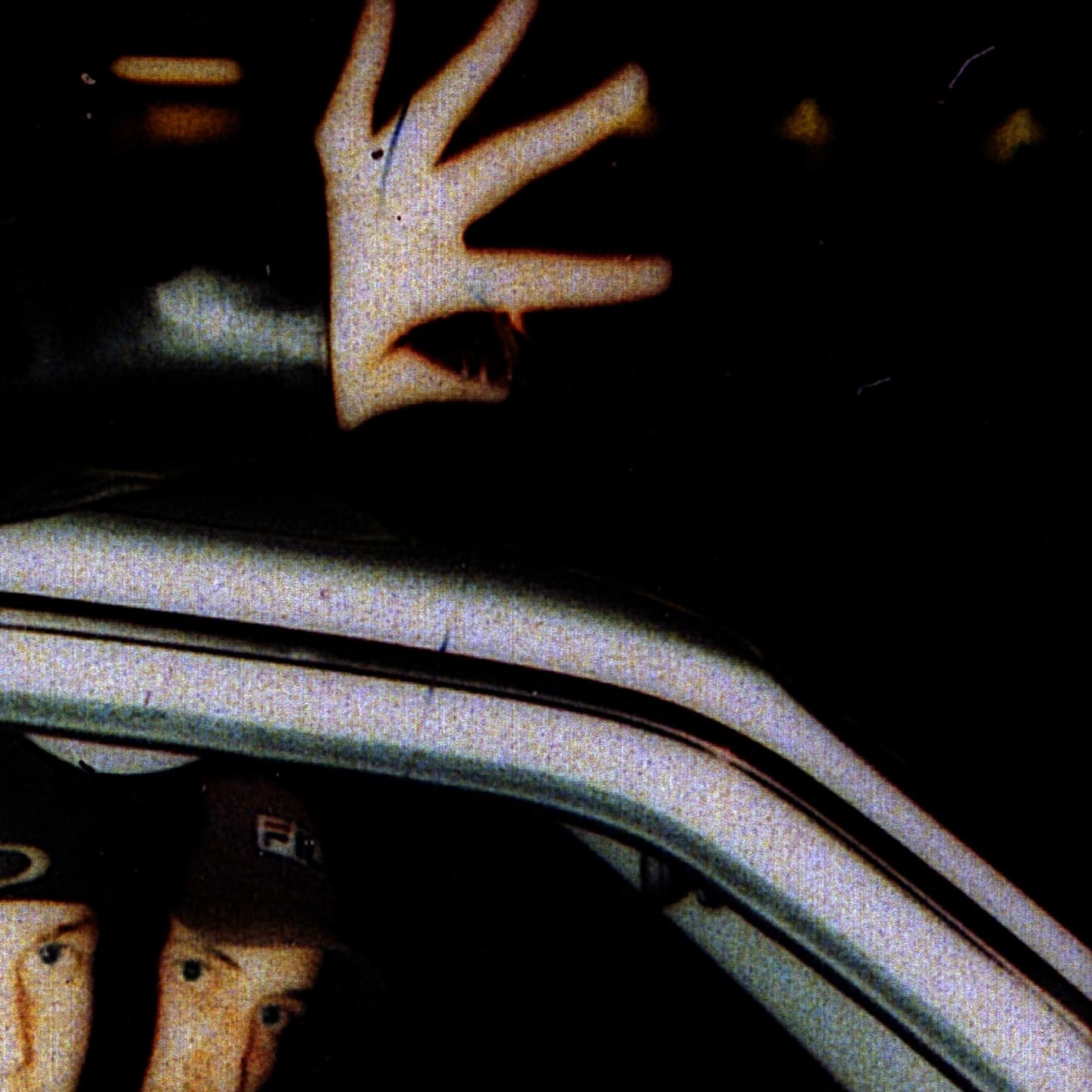 Close-up shows two men partially visible inside a car at night, with one man's hand seen near the roof of the vehicle.