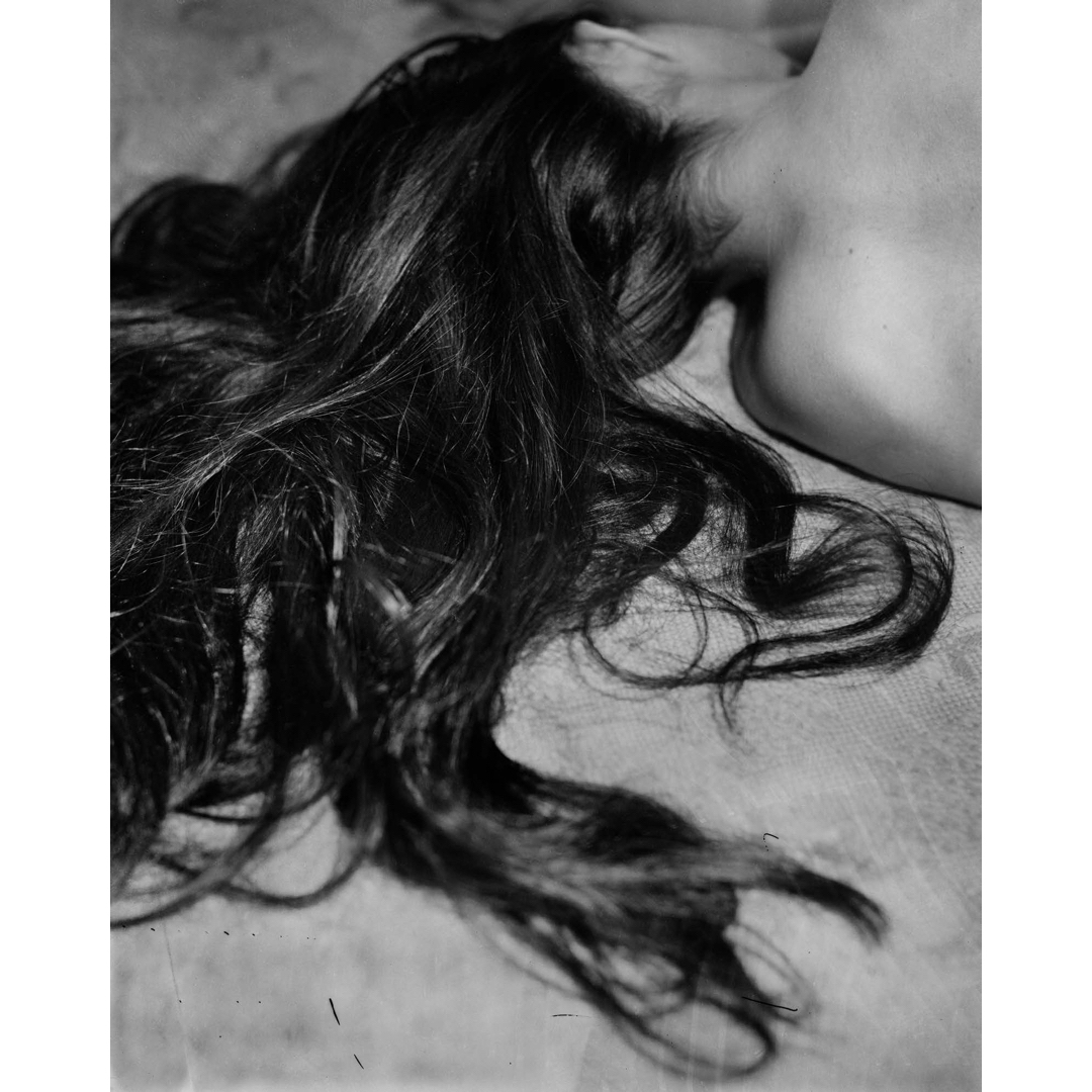Black and white shot of a dark-haired female lying down, showcasing her hair's texture and form against a light-colored textured surface.