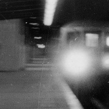 Grayscale photograph of a blurry train arriving at a dimly lit Paris station platform captured by Jh Engström