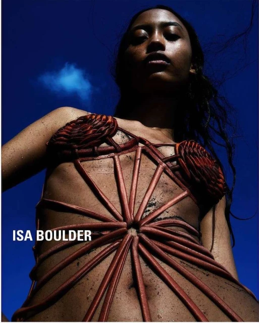 Fashion portrait of a woman wearing a structural dress with a blue sky background, taken with a low-angle perspective.