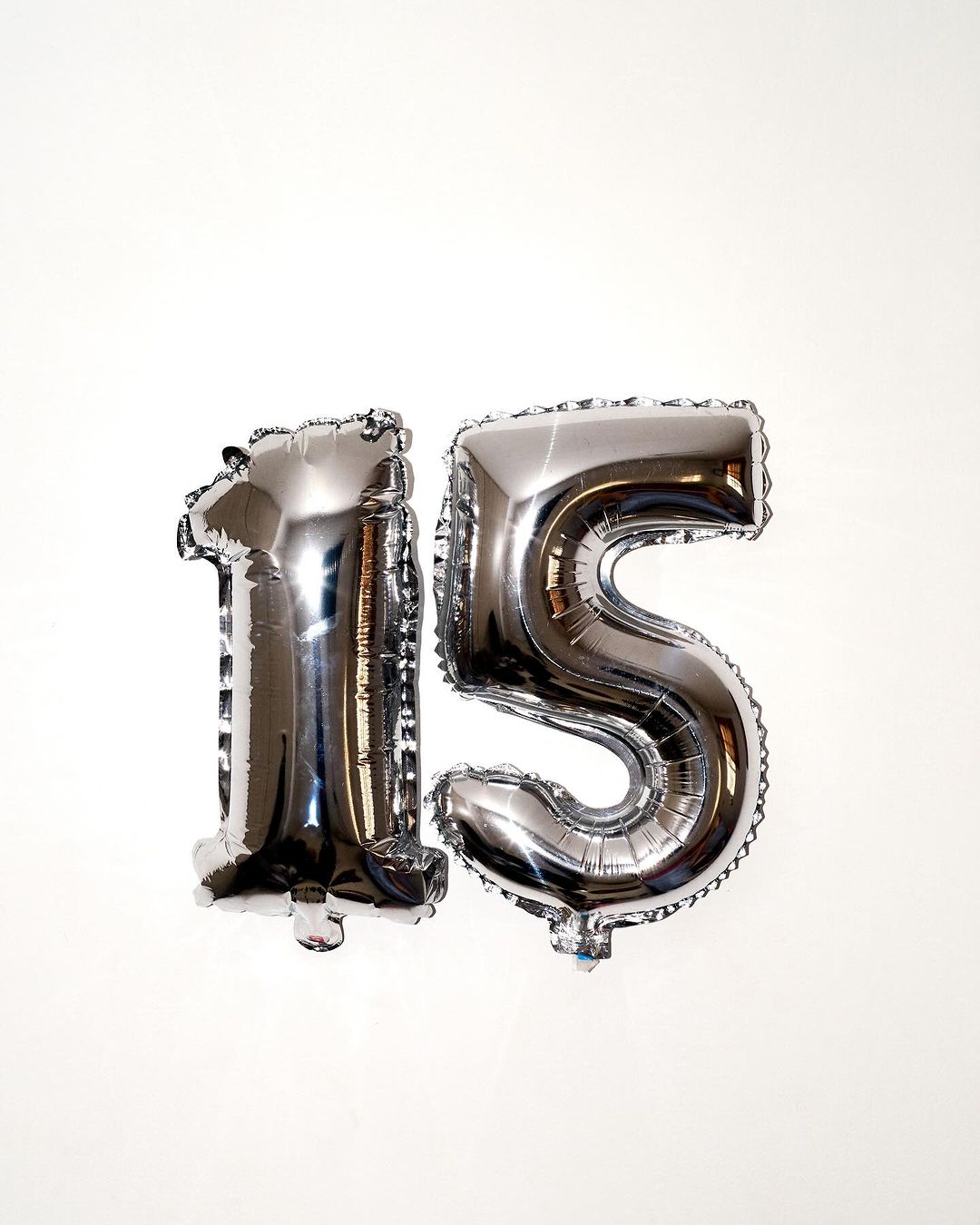Shiny silver foil balloons shaped like the number 15 against a plain white background. Party decoration, celebration, milestone birthday.