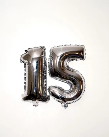 Shiny silver foil balloons shaped like the number 15 against a plain white background. Party decoration, celebration, milestone birthday.