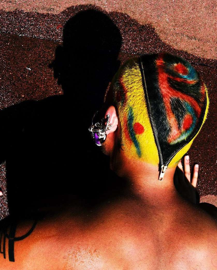 Close-up of adult with dyed yellow hair, multi-colored design, and zipper detail, accessorized with a unique metal ear adornment.