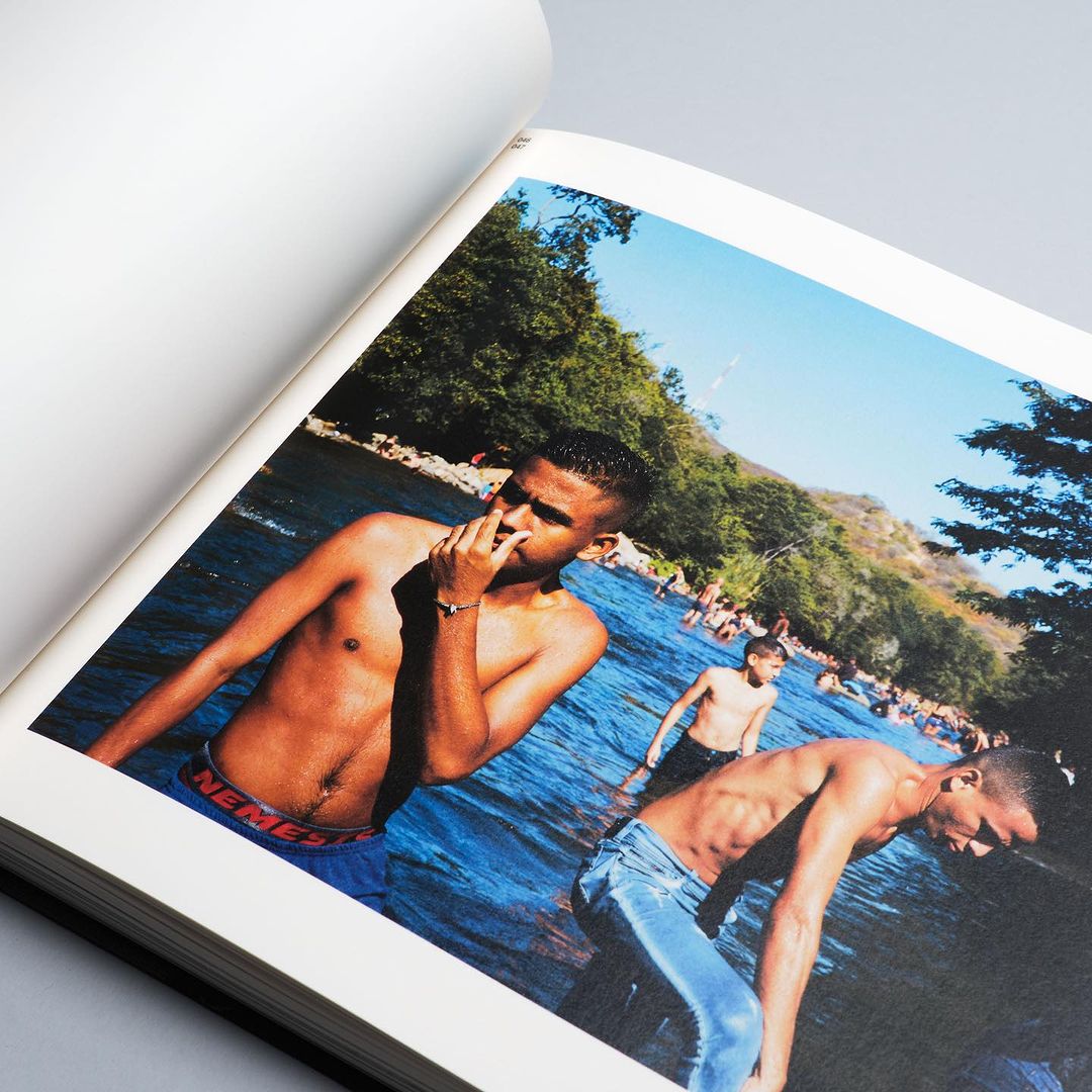 Photograph from a book shows three shirtless young men standing in a river surrounded by lush vegetation on a sunny day.