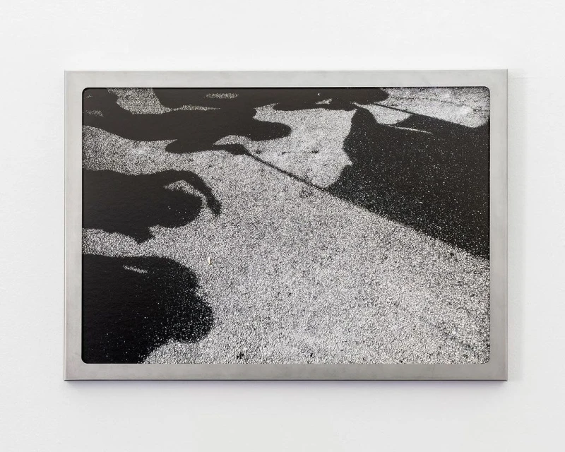 High-angle black-and-white photographic art print in a silver frame, showing dark human shadows on a grainy gray sidewalk.