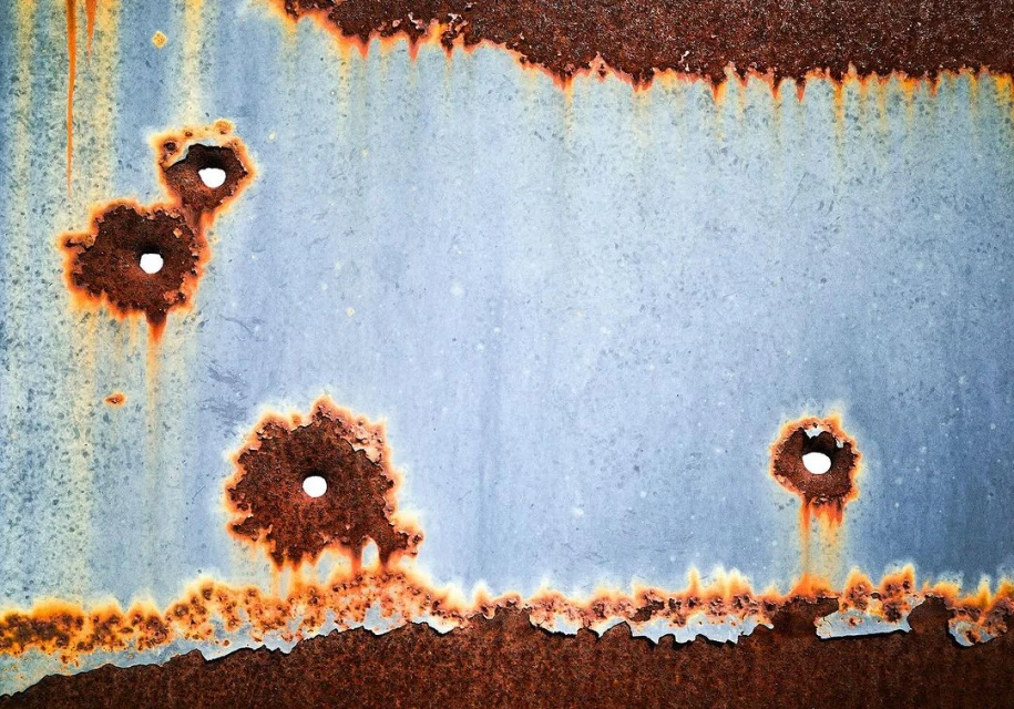 Close-up shot of weathered metal sheet with rust and holes, showcasing the texture and decay of the aged material.