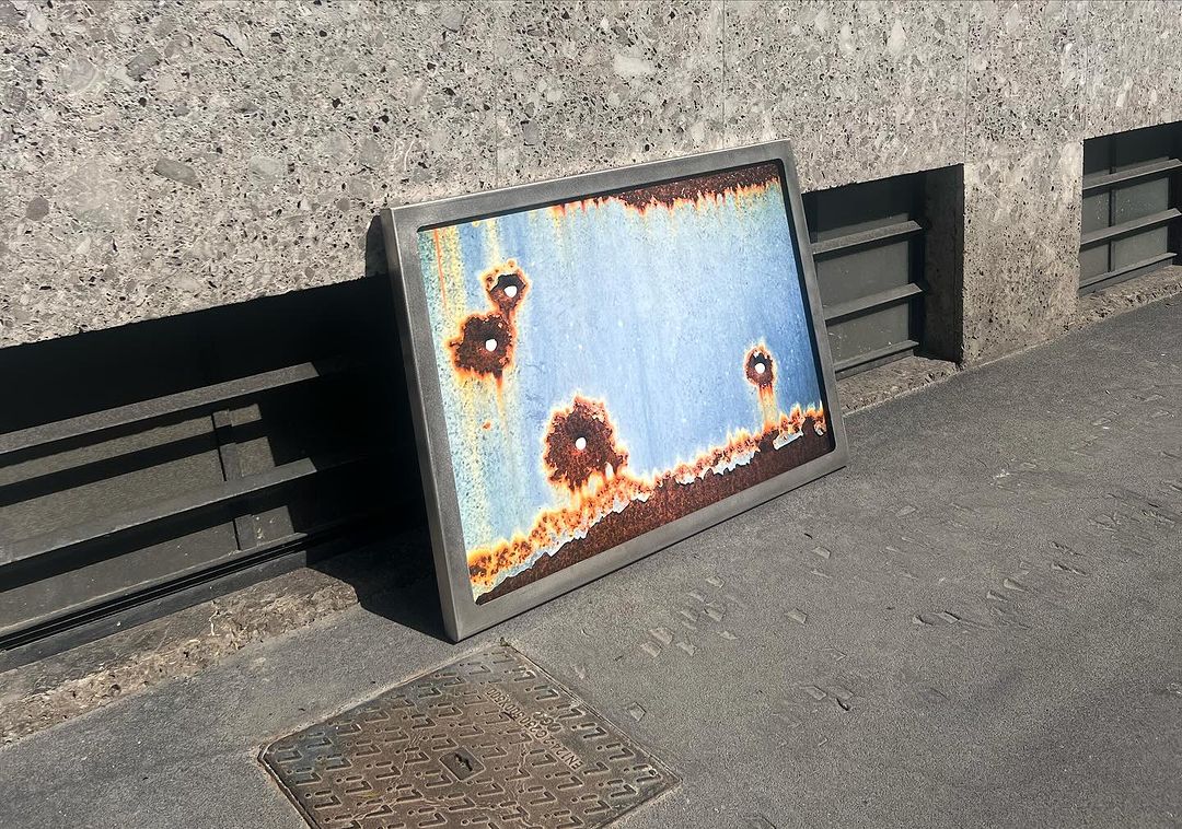 Image featuring rusted metal in a silver frame leaning against a grey concrete wall, creating an abstract and weathered aesthetic.