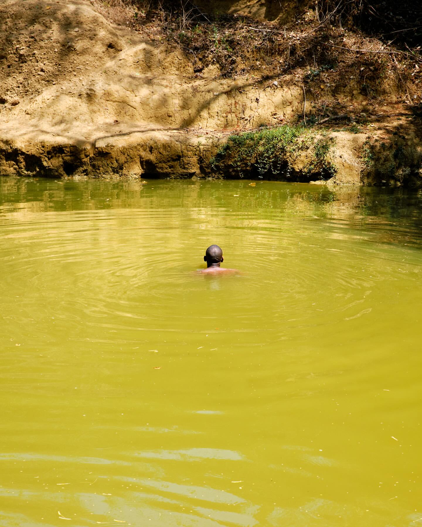 Man swimming in a body of water surrounded by a rocky, vegetated cliffside under natural light, creating ripples on the water's surface.