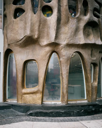 Architectural detail of an organically-shaped building with irregularly-placed windows and a view of an office inside.