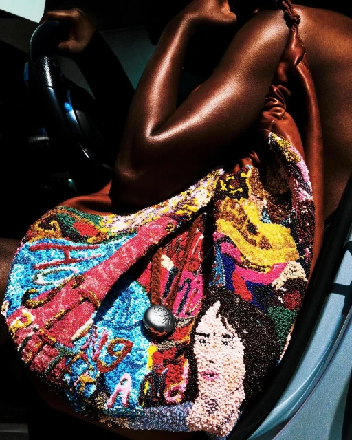 Close-up shot of a woman's arm and shoulder holding a colorful beaded handbag in a car; the bag features a portrait design.