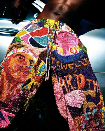 Close-up portrait of a shirtless man wearing brightly colored graphic patterned textured trousers leaning against a car.