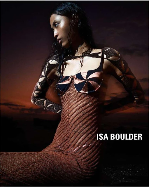 Fashion shot of a Black woman wearing a patterned dress against a sunset background, showcasing clothing by ISA BOULDER.