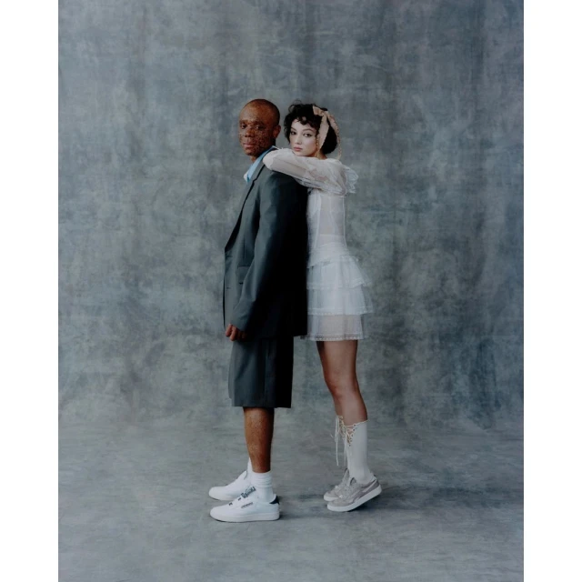 Studio shot of an adult African American man and a young fair-skinned woman in a modern fashion pose, set against a grey background.