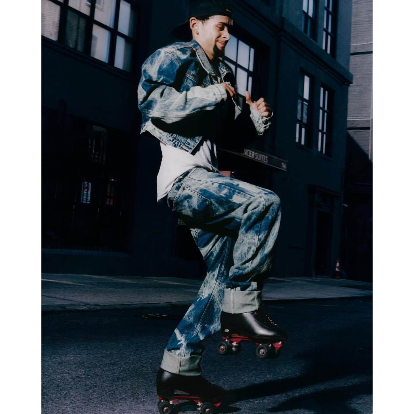 Young adult roller skating on a city street at night, wearing a baseball cap, denim jacket and jeans, captured in an eye-level shot.