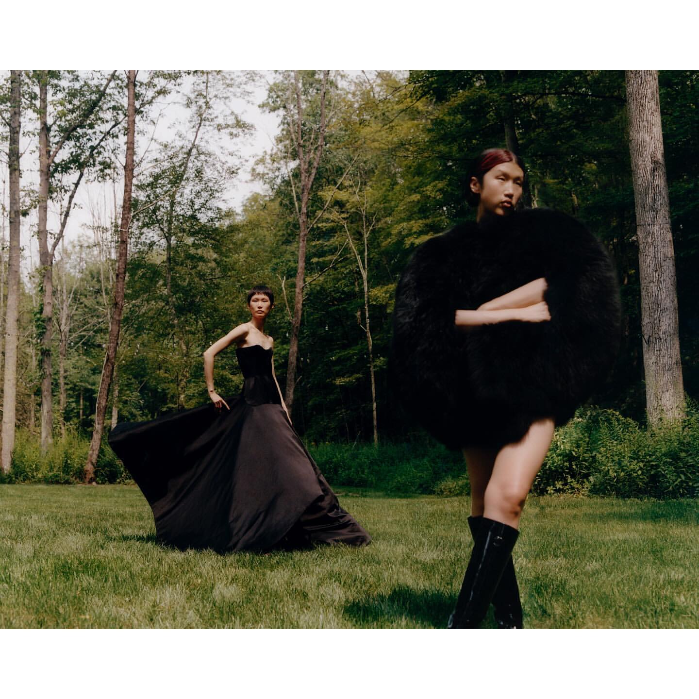 Two models posing outdoors in a wooded forest clearing, wearing black garments photographed by Jingyu Lin.