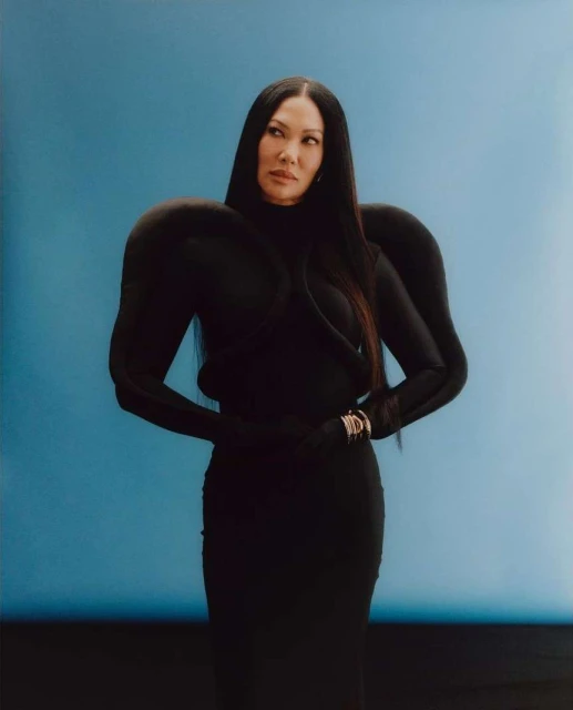 Elegant portrait of an Asian woman in a black dress with bold shoulders against a vibrant blue backdrop in a studio setting.