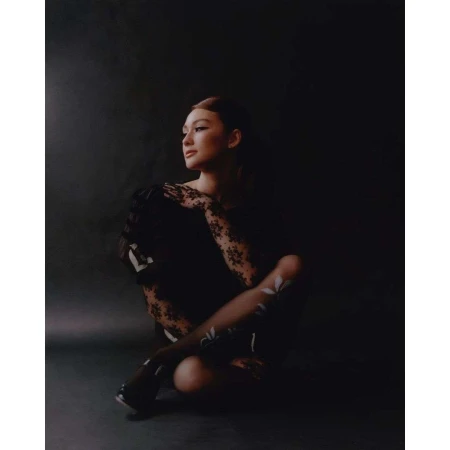 Portrait of a woman with lace gloves and floral-patterned tights, sitting indoors in dark, moody lighting, looking off-camera.