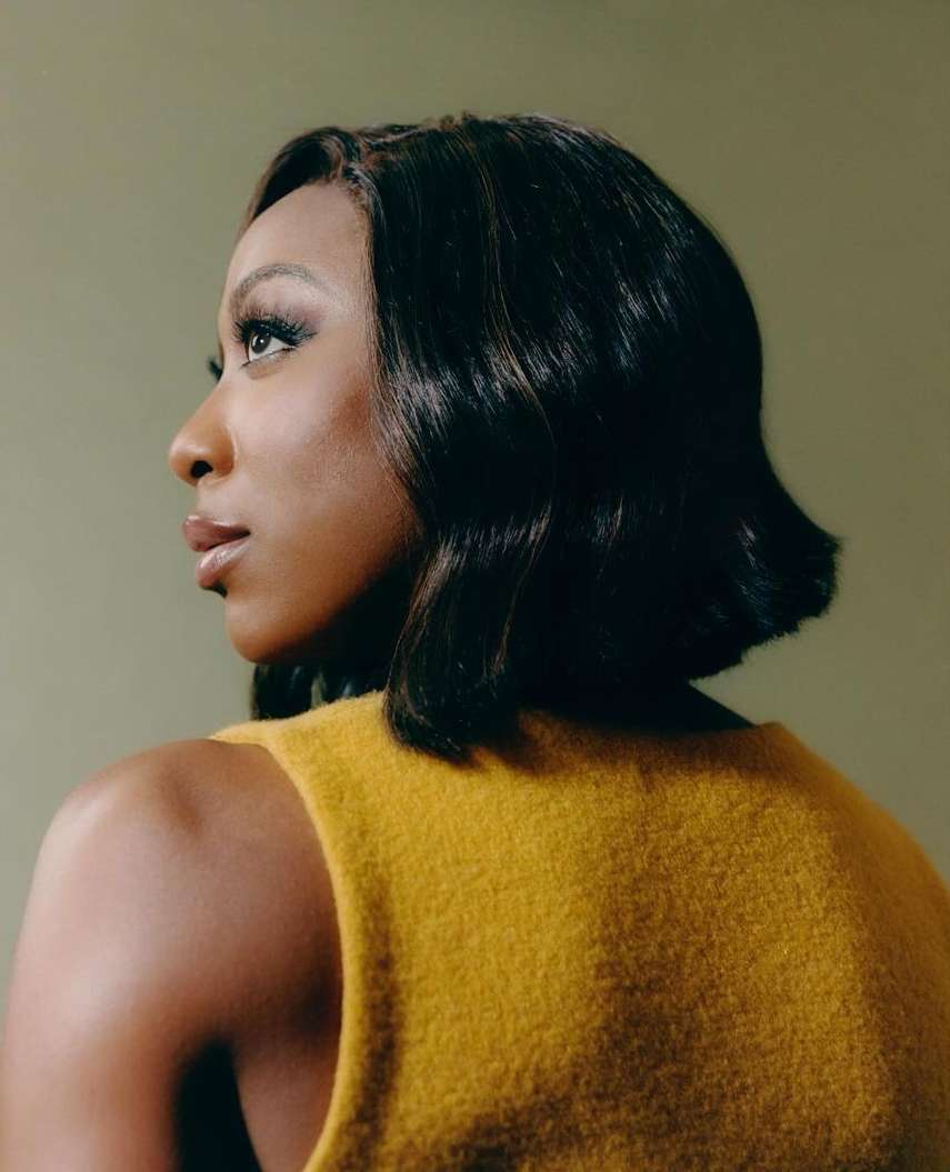 Portrait of an African-American adult female looking over her shoulder wearing a gold-colored top with a green-toned background.