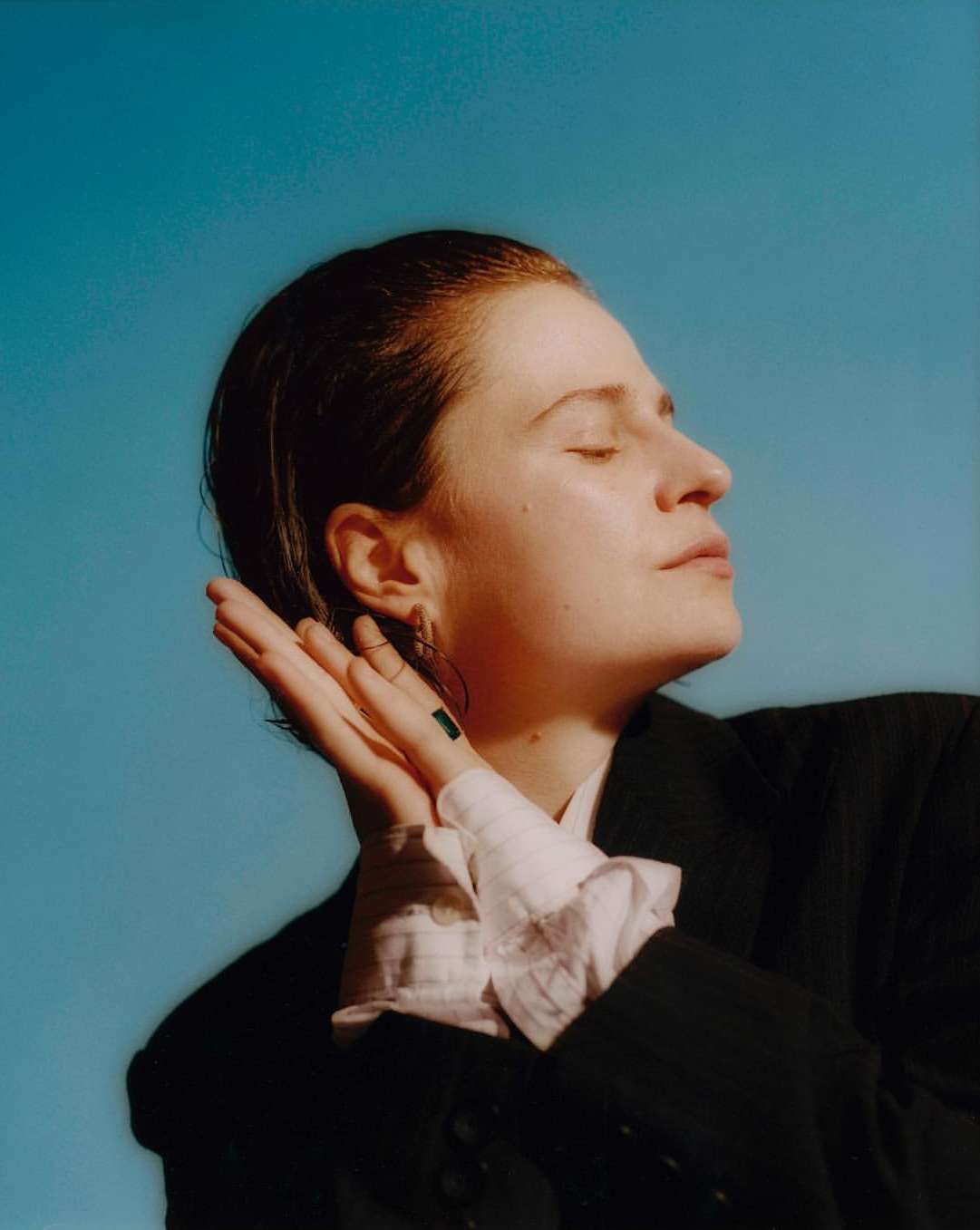Close-up studio portrait of a fair-skinned woman with short reddish hair posing against a clear blue background with natural light.