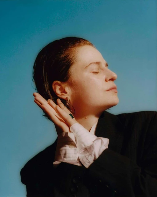 Close-up studio portrait of a fair-skinned woman with short reddish hair posing against a clear blue background with natural light.