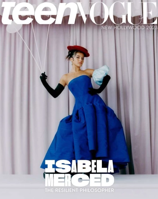 Teen Vogue cover with Isabela Merced wearing a blue dress, black gloves, and a red hat, holding balloons, against a curtain backdrop.