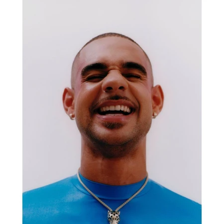 Close-up portrait of a smiling man wearing a blue top and a silver animal pendant necklace against a light background.