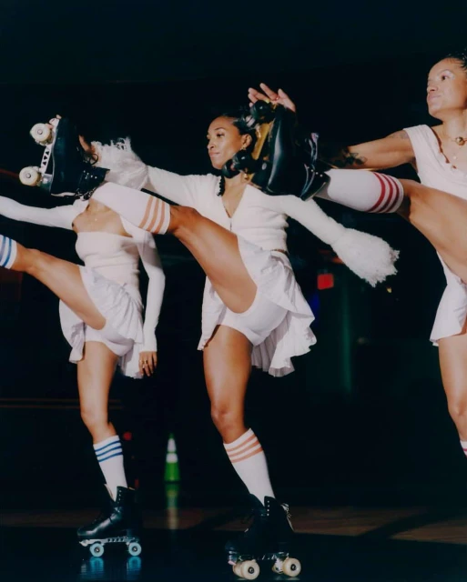 Three women on roller skates strike a pose, wearing matching outfits and striped socks against a dark background. 