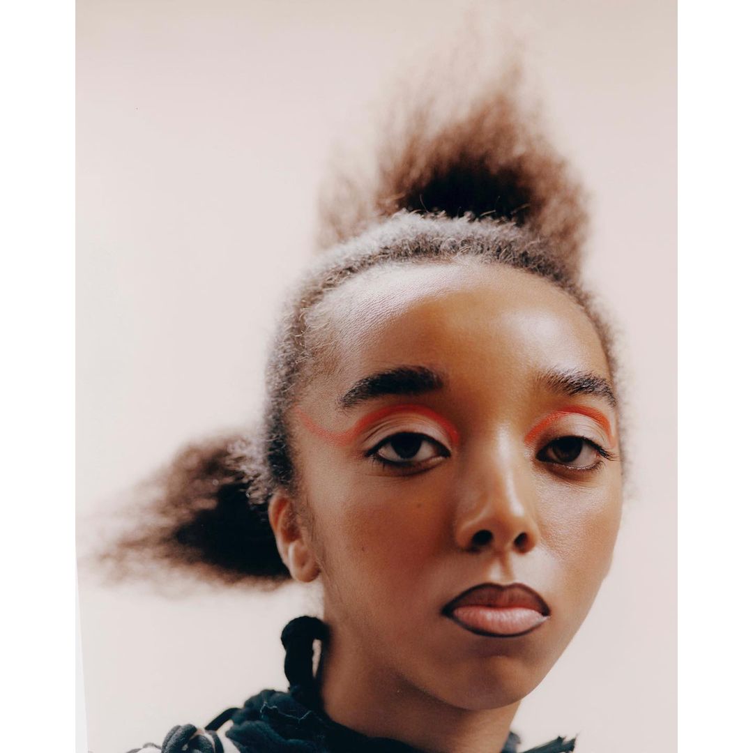 Close-up portrait of a young woman with creative makeup, featuring bright red eyeshadow, strong black eyeliner and artistic hair styling.