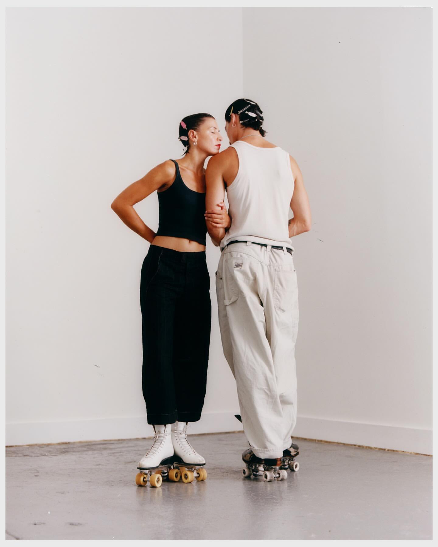Indoor shot of a couple in casual clothing, standing on roller skates. The woman is leaning in with her eyes closed.