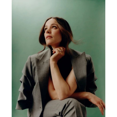 Woman in a grey blazer with ruffled sleeves posing against a solid green background