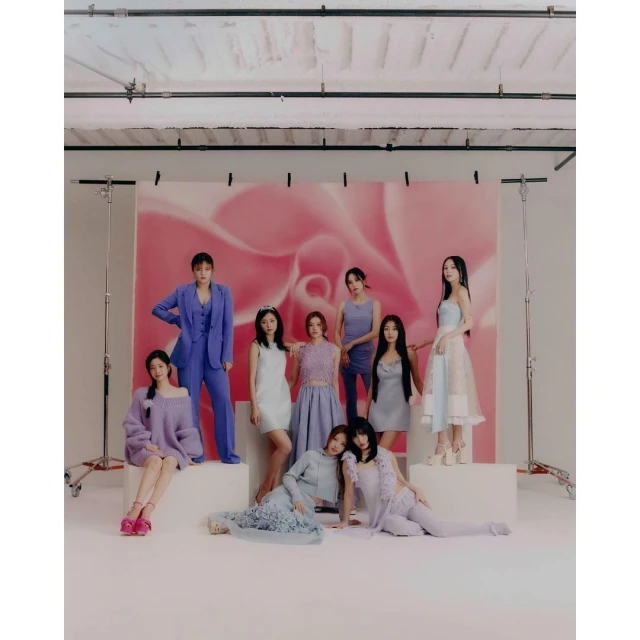A group of nine young women pose in a studio wearing light-colored dresses and suits in a fashion editorial, studio lighting.