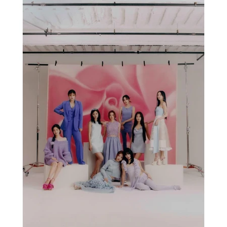 A group of nine young women pose in a studio wearing light-colored dresses and suits in a fashion editorial, studio lighting.