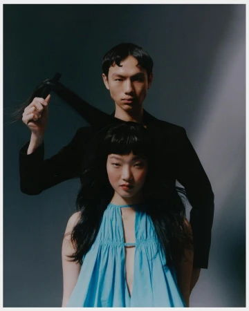 Two models posing with a man holding a strand of hair against a dark gradient background in a fashion portrait by Jingyu Lin
