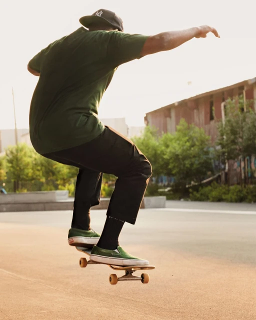 Skateboarder in mid-air performing a trick at skatepark, wearing dark green t-shirt, black pants, and baseball cap.