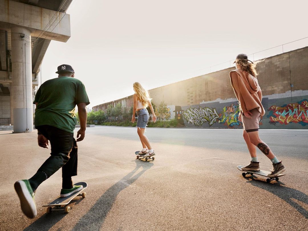 Three young adults skateboarding in an urban setting with graffiti art and architectural elements in the background during daytime.