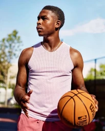 Black man wearing a pink mesh tank top holding a basketball outdoors under a clear sky.