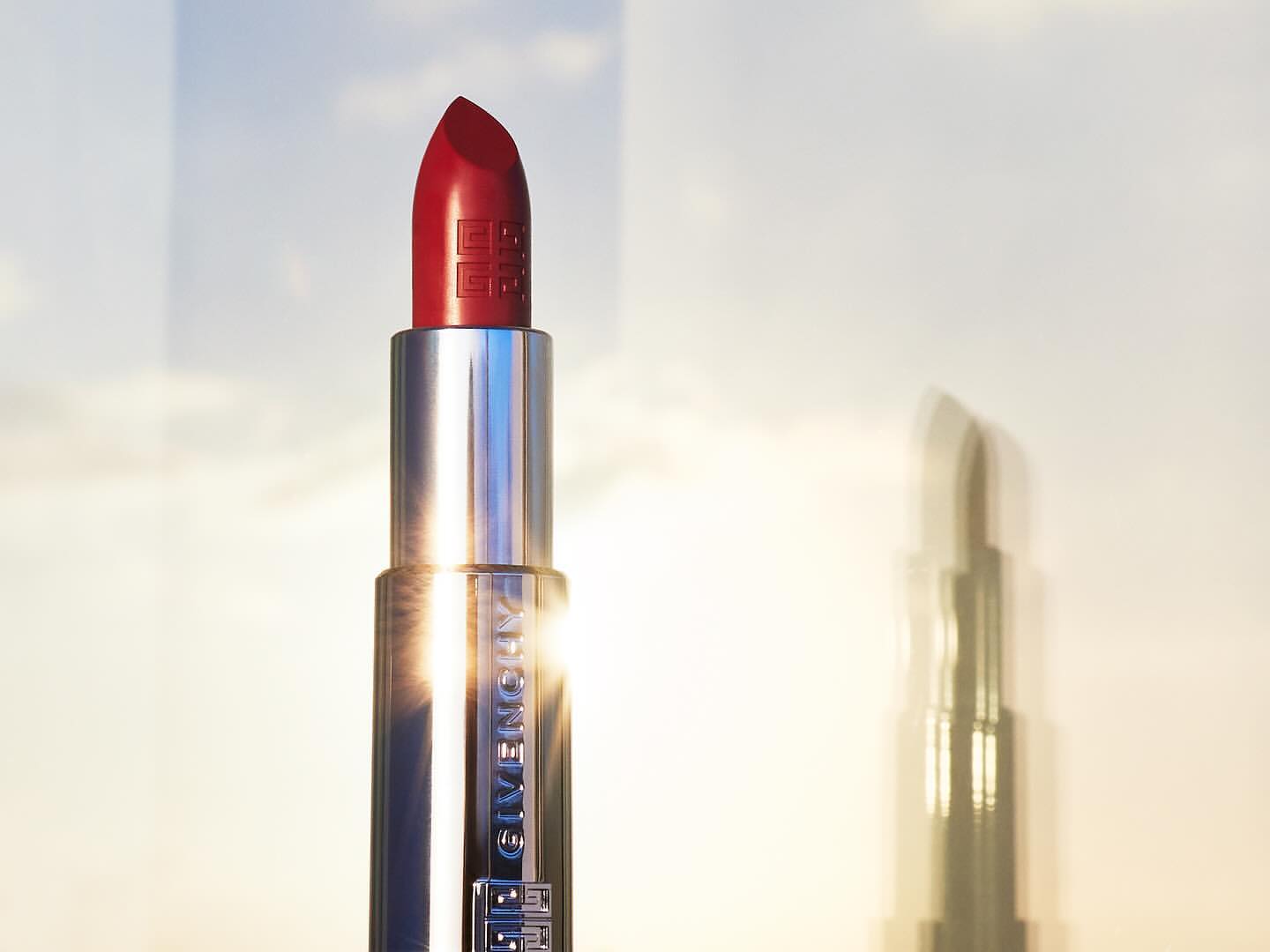 Close-up studio shot of a vibrant red lipstick in a silver tube against a dreamy sky, highlighting the beauty and luxury.