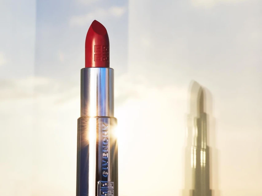 Close-up studio shot of a vibrant red lipstick in a silver tube against a dreamy sky, highlighting the beauty and luxury.