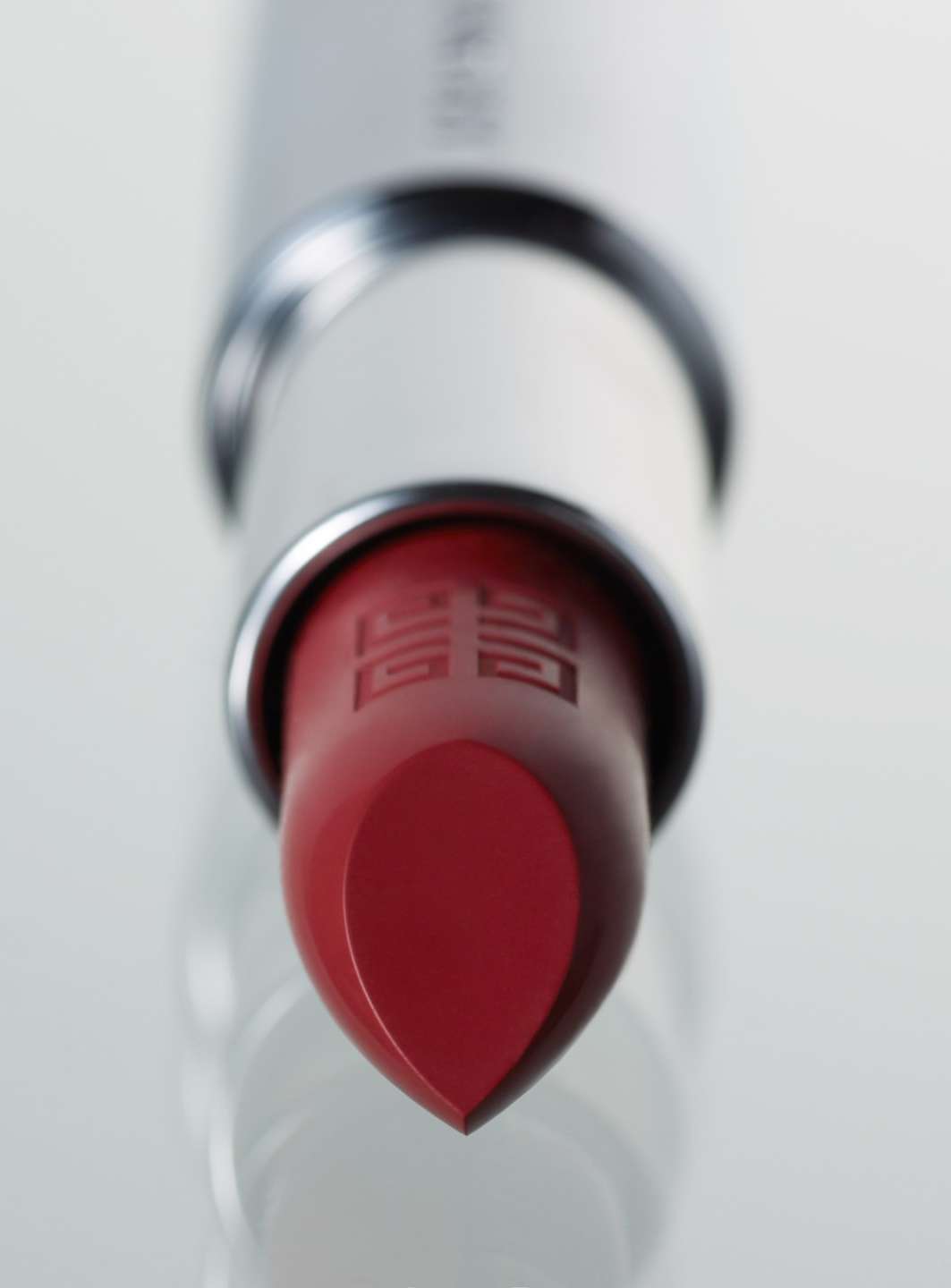 Close-up studio shot of red lipstick with brand logo on a reflective white surface. Makeup, cosmetic product, beauty industry, studio lighting.