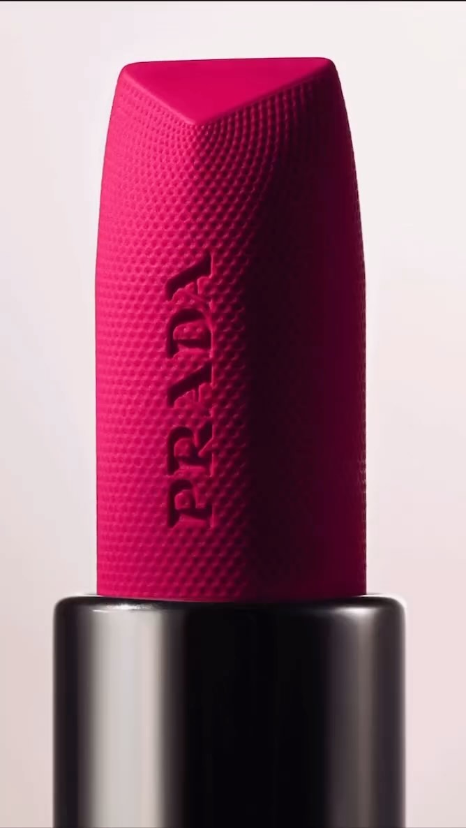 Close-up studio shot of Prada lipstick in a black tube with a raspberry matte texture and the brand name embossed on the side.