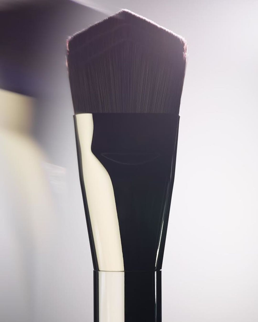 Close-up studio shot of a makeup brush featuring dark brown bristles and a black handle with a luminous white background.