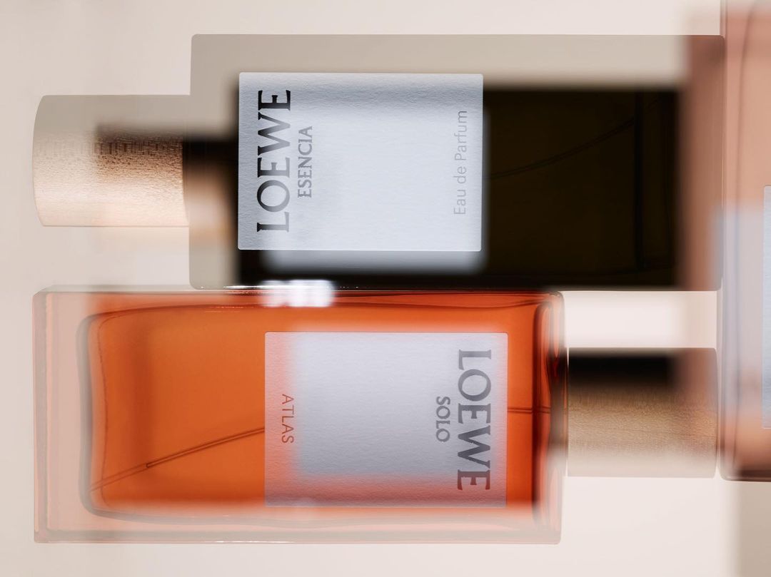 Overhead shot of two Loewe perfume bottles, one amber and one dark, featuring minimal labels on a neutral, blurred background.