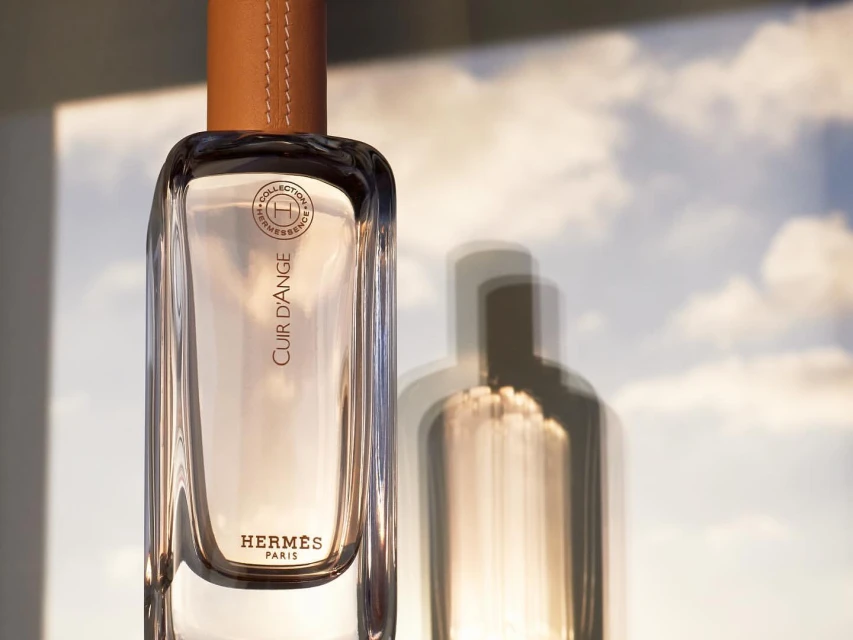 Product shot of Hermès Cuir d'Ange perfume bottle with leather top, set against a soft sky background, showcasing luxury and simplicity.